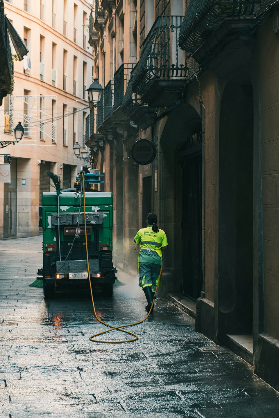 Un addetto alle pulizie pulisce una strada acciottolata con un'idropulitrice.